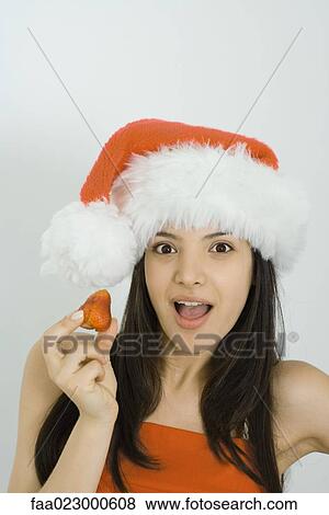 Young woman wearing Santa hat, holding up strawberry, looking at camera, open mouth View Large Photo Image Stock Photo - Young woman wearing Santa hat, holding up strawberry, looking at camera, open mouth. Fotosearch