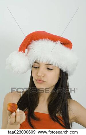 Stock Photo - Young woman wearing Santa hat, looking down at strawberry. Fotosearch