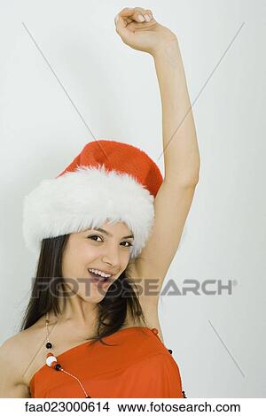 Young woman wearing Santa hat, smiling at camera, arm raised, portrait View Large Photo Image Picture - Young woman wearing Santa hat, smiling at camera, arm raised, portrait. Fotosearch