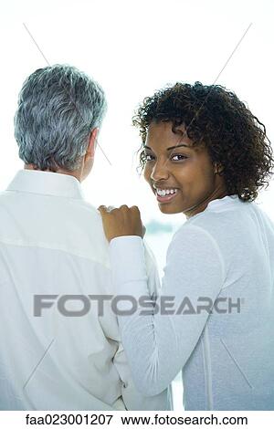 Stock Photo - Young woman with hand on mature man's shoulder, woman looking over shoulder at camera. Fotosearch
