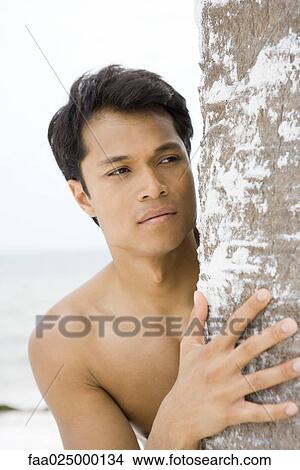 Barechested man looking around tree trunk, close-up View Large Photo Image Picture - Barechested man looking around tree trunk, close-up. Fotosearch