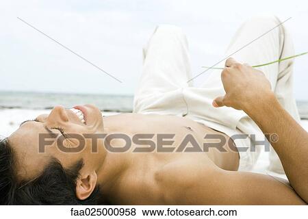 Barechested man lying on sand, holding blade of grass, laughing View Large Photo Image Stock Photo - Barechested man lying on sand, holding blade of grass, laughing. Fotosearch