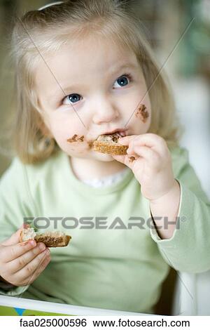 Stock Photograph - Blonde toddler girl eating bread with chocolate. Fotosearch