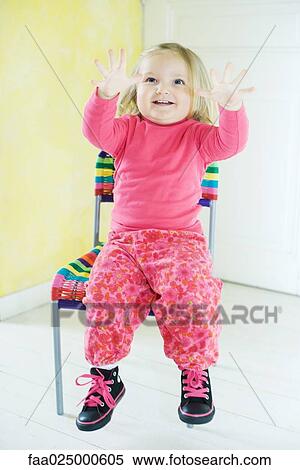 Stock Photography - Blonde toddler girl sitting in chair, holding up fingers. Fotosearch