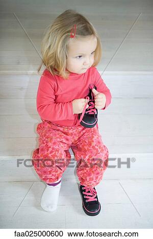 Blonde toddler girl sitting on steps, wearing one shoe, holding other shoe in hand View Large Photo Image Stock Image - Blonde toddler girl sitting on steps, wearing one shoe, holding other shoe in hand. Fotosearch