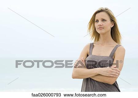 Blonde woman standing with arms folded, sea in background, waist up View Large Photo Image Stock Image - Blonde woman standing with arms folded, sea in background, waist up. Fotosearch