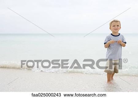 Boy at the beach, standing ankle deep in water, looking up and smiling View Large Photo Image Stock Image - Boy at the beach, standing ankle deep in water, looking up and smiling. Fotosearch