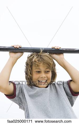 Boy hanging from metal bar, smiling, cropped view View Large Photo Image Stock Image - Boy hanging from metal bar, smiling, cropped view. Fotosearch