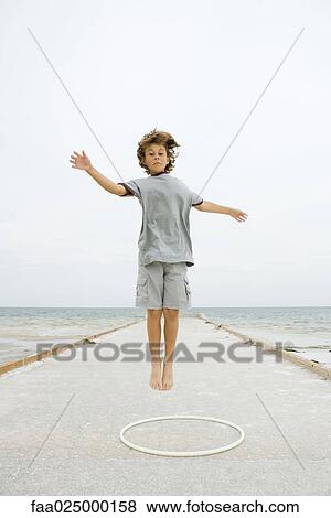 Boy jumping over plastic hoop with arms out, looking at camera View Large Photo Image Stock Photo - Boy jumping over plastic hoop with arms out, looking at camera. Fotosearch