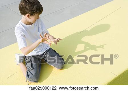 Boy kneeling on the ground, making shadow figures with hands, high angle view View Large Photo Image Stock Image - Boy kneeling on the ground, making shadow figures with hands, high angle view. Fotosearch