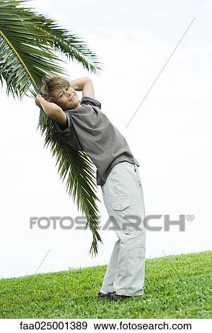 Boy leaning against palm branch, smiling at camera View Large Photo Image Stock Photo - Boy leaning against palm branch, smiling at camera. Fotosearch