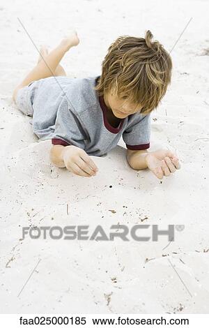Boy lying on stomach in sand with legs up, looking down View Large Photo Image Stock Photography - Boy lying on stomach in sand with legs up, looking down. Fotosearch