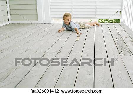 Stock Image - Boy lying on stomach on the ground, lining up pebbles. Fotosearch