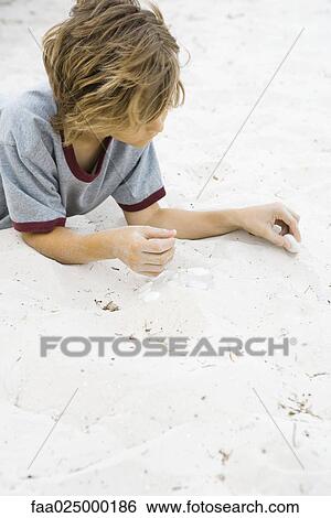 Boy lying on the ground, arranging pebbles in sand View Large Photo Image Stock Photograph - Boy lying on the ground, arranging pebbles in sand. Fotosearch