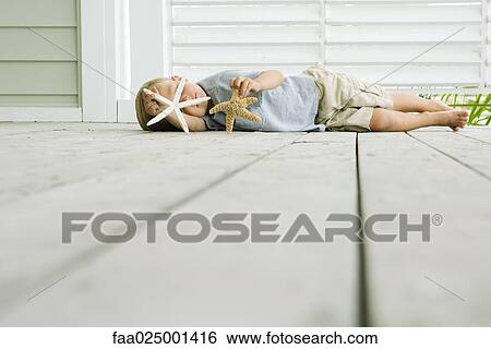 Boy lying on the ground holding two starfish View Large Photo Image Stock Photograph - Boy lying on the ground holding two starfish. Fotosearch