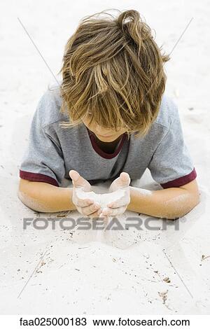 Boy lying on the ground, looking down at handful of sand View Large Photo Image Stock Image - Boy lying on the ground, looking down at handful of sand. Fotosearch