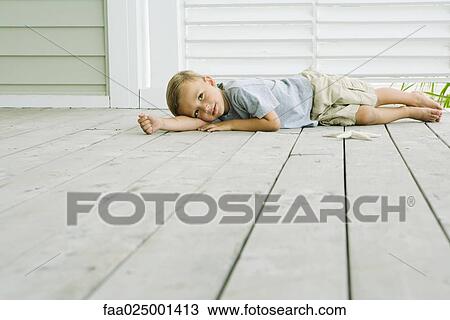 Stock Image - Boy lying on the ground next to starfish, head resting on arm. Fotosearch
