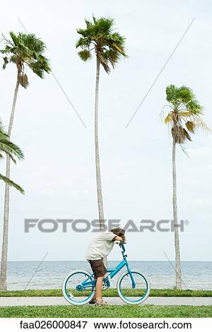 Boy on bicycle at the beach, head resting on arms, side view View Large Photo Image Stock Photo - Boy on bicycle at the beach, head resting on arms, side view. Fotosearch