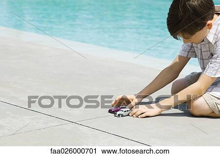 Boy sitting on ground, playing with toy cars, next to pool View Large Photo Image Stock Image - Boy sitting on ground, playing with toy cars, next to pool. Fotosearch