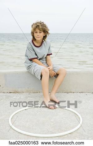 Boy sitting on low wall at the beach, foot touching plastic hoop View Large Photo Image Stock Image - Boy sitting on low wall at the beach, foot touching plastic hoop. Fotosearch