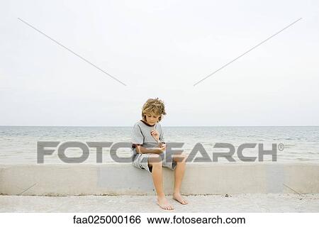 Boy sitting on low wall at the beach, looking down at starfish View Large Photo Image Stock Photograph - Boy sitting on low wall at the beach, looking down at starfish. Fotosearch
