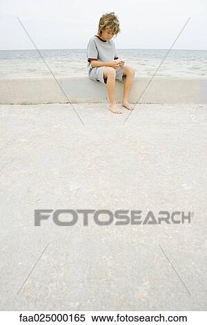 Boy sitting on low wall at the beach, looking down at starfish View Large Photo Image Stock Photography - Boy sitting on low wall at the beach, looking down at starfish. Fotosearch