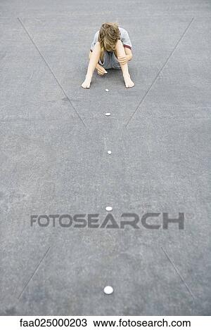 Boy sitting on the ground arranging line of pebbles, high angle view View Large Photo Image Stock Image - Boy sitting on the ground arranging line of pebbles, high angle view. Fotosearch