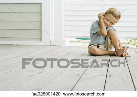 Boy sitting on the ground listening to seashell, squinting at camera, smiling View Large Photo Image Stock Image - Boy sitting on the ground listening to seashell, squinting at camera, smiling. Fotosearch