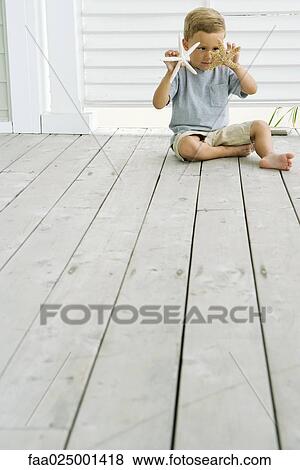 Boy sitting on the ground, looking at starfish in hand View Large Photo Image Stock Photo - Boy sitting on the ground, looking at starfish in hand. Fotosearch