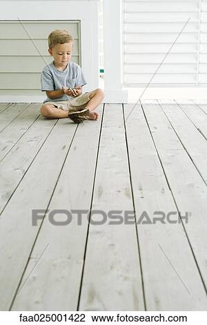 Stock Image - Boy sitting on the ground next to bird's nest, looking down at eggs in his hands. Fotosearch