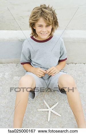 Boy sitting on the ground next to starfish, smiling up at camera View Large Photo Image Stock Photo - Boy sitting on the ground next to starfish, smiling up at camera. Fotosearch