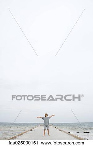Boy standing on pier at mid-distance, arms out View Large Photo Image Stock Image - Boy standing on pier at mid-distance, arms out. Fotosearch