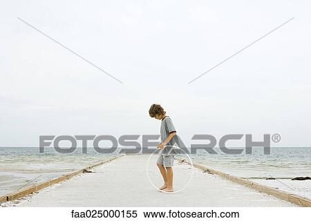 Boy standing on pier holding plastic hoop, looking down, side view View Large Photo Image Stock Photography - Boy standing on pier holding plastic hoop, looking down, side view. Fotosearch