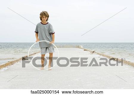 Boy standing on pier playing with plastic hoop, full length View Large Photo Image Picture - Boy standing on pier playing with plastic hoop, full length. Fotosearch