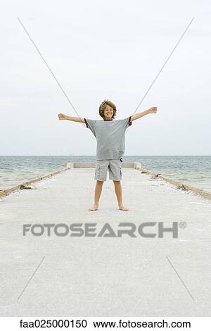 Boy standing on pier with arms out and eyes closed, front view View Large Photo Image Stock Image - Boy standing on pier with arms out and eyes closed, front view. Fotosearch