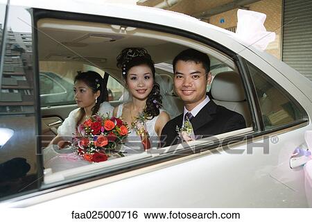 Stock Photograph - Bride and groom in car with bridesmaid, smiling at camera. Fotosearch