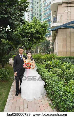 Bride and groom standing in verdant apartment complex, full length portrait View Large Photo Image Stock Photo - Bride and groom standing in verdant apartment complex, full length portrait. Fotosearch