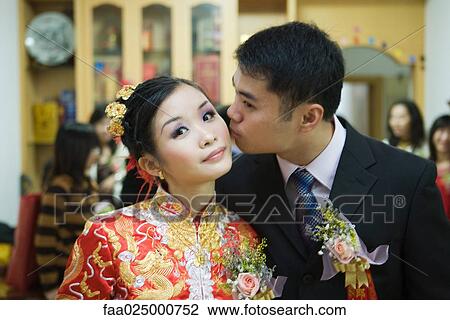 Bride dressed in traditional Chinese clothing, looking at camera as groom kisses her on the cheek View Large Photo Image Stock Image - Bride dressed in traditional Chinese clothing, looking at camera as groom kisses her on the cheek. Fotosearch