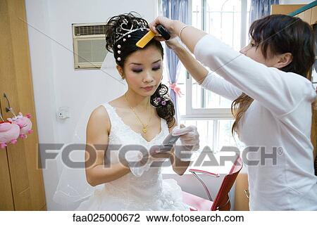 Stock Image - Bride having her hair styled by friend, looking down at cell phone. Fotosearch