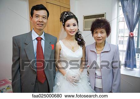 Stock Image - Bride standing between parents, smiling at camera, portrait. Fotosearch