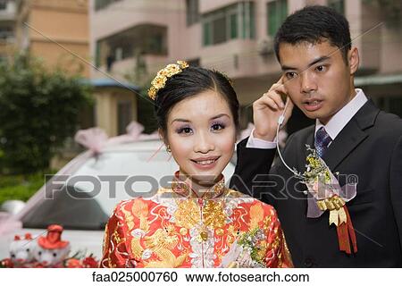 Bride wearing traditional Chinese clothing, smiling at camera, groom behind using earphone View Large Photo Image Stock Image - Bride wearing traditional Chinese clothing, smiling at camera, groom behind using earphone. Fotosearch