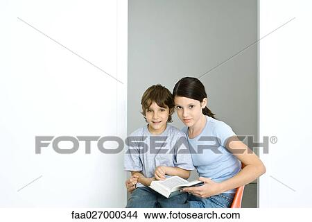 Brother and sister sitting together, girl holding book, both looking at camera View Large Photo Image Picture - Brother and sister sitting together, girl holding book, both looking at camera. Fotosearch