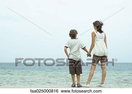 Brother and sister standing at the beach holding hands, looking at view View Large Photo Image Stock Photograph - Brother and sister standing at the beach holding hands, looking at view. Fotosearch