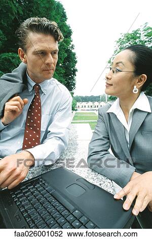 Business associates sitting outdoors, looking at each other, woman using laptop computer View Large Photo Image Stock Image - Business associates sitting outdoors, looking at each other, woman using laptop computer. Fotosearch