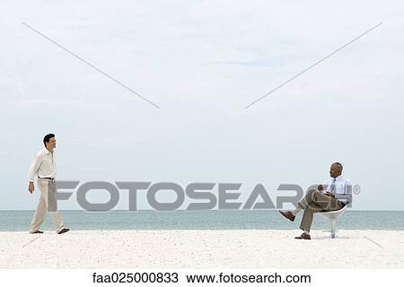 Businessman at the beach walking toward seated colleague, both smiling View Large Photo Image Stock Image - Businessman at the beach walking toward seated colleague, both smiling. Fotosearch
