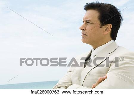 Businessman crossing arms, looking at distance, sea in background View Large Photo Image Stock Image - Businessman crossing arms, looking at distance, sea in background. Fotosearch