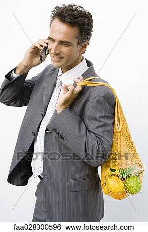 Businessman holding reusable grocery bag over shoulder, using cell phone View Large Photo Image Stock Photograph - Businessman holding reusable grocery bag over shoulder, using cell phone. Fotosearch