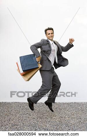 Businessman holding shopping bags, jumping in midair, full length View Large Photo Image Picture - Businessman holding shopping bags, jumping in midair, full length. Fotosearch
