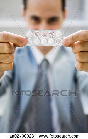 Businessman holding up package of tablets, looking at camera, focus on foreground View Large Photo Image Stock Image - Businessman holding up package of tablets, looking at camera, focus on foreground. Fotosearch