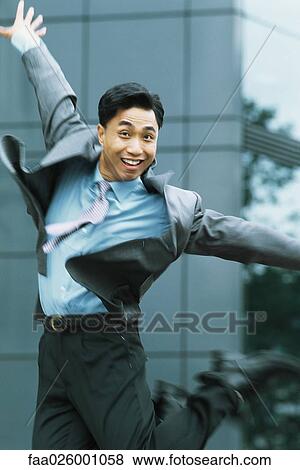 Stock Photo - Businessman jumping in the air, arms out, smiling at camera. Fotosearch